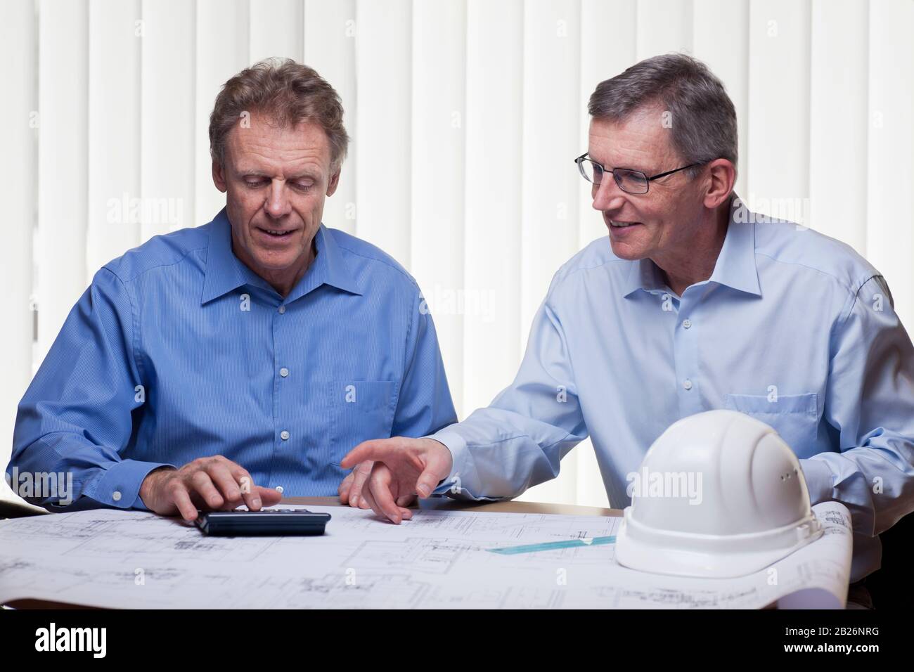 Zwei ausgereifte Architekten oder Ingenieure kalutieren ein Projekt an einem Schreibtisch mit Blaupause Stockfoto