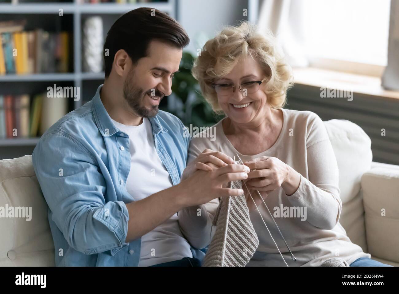 Glückliche ältere Mutter lehrt den strickenden erwachsenen Sohn Stockfoto