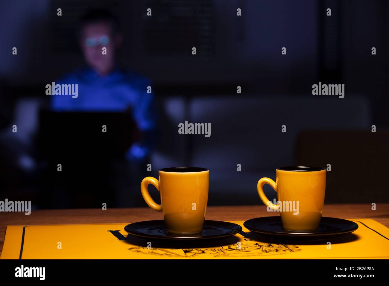 Zwei Tassen Kaffee auf einem Tisch und Mann mit Laptop auf einer Couch im Hintergrund Stockfoto