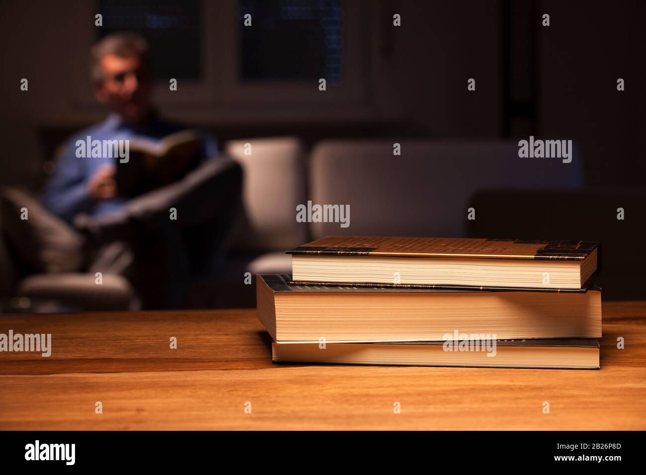 Reifer Mann liest nachts ein Buch im Wohnzimmer - im Vordergrund stehen die Bücher Stockfoto