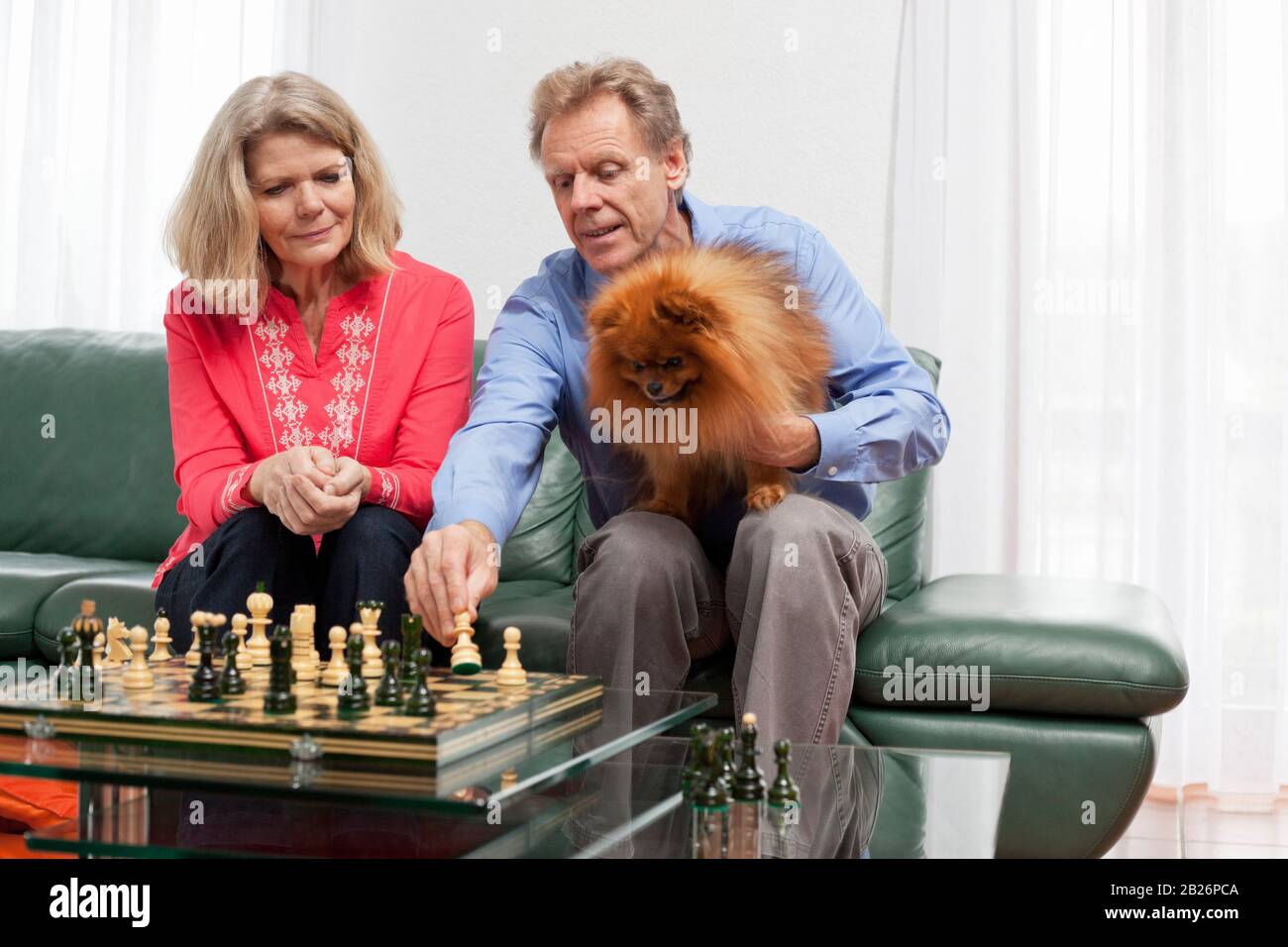 Reifes lächelndes Paar, das in einem hellen Wohnzimmer Schach spielt Stockfoto