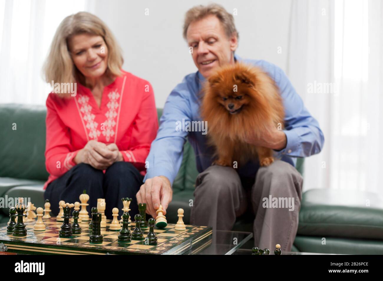 Reifes lächelndes Paar, das in einem hellen Wohnzimmer Schach spielt - konzentrieren Sie sich auf das Schachbrett im Vordergrund Stockfoto