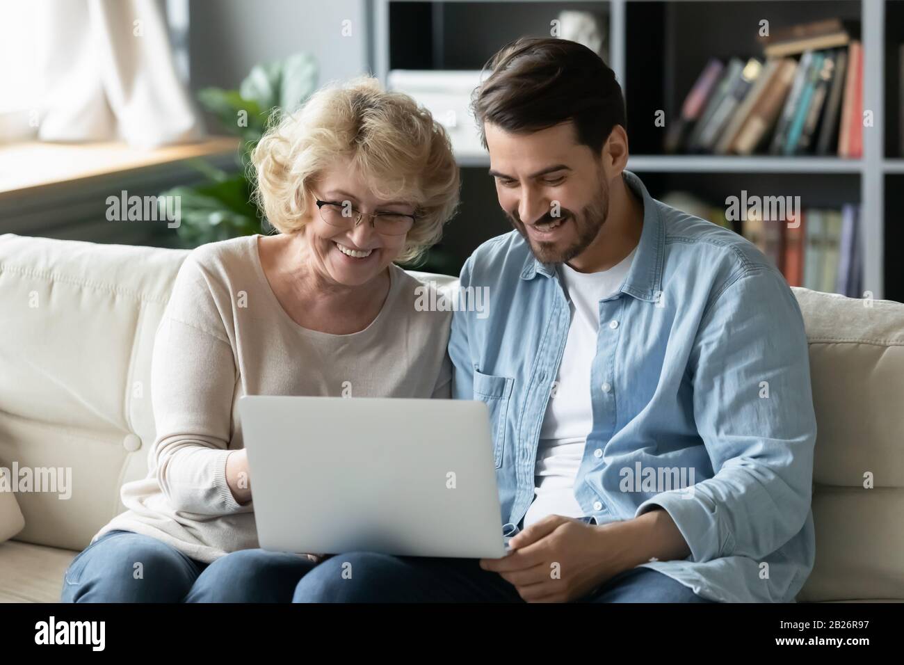 Eine glückliche ältere Mutter und ein erwachsener Sohn, die zu Hause einen Laptop benutzen Stockfoto