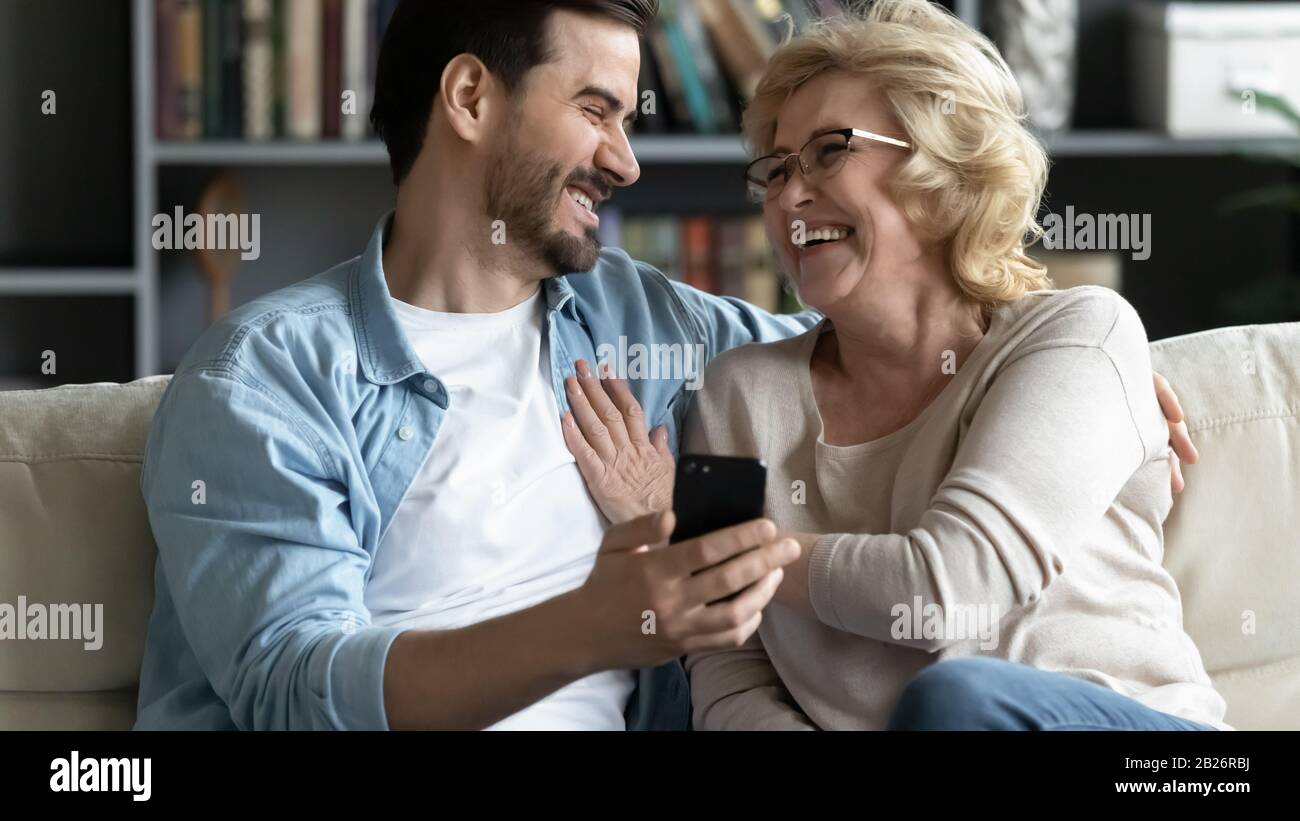 Überfreute ältere Mutter und erwachsener Sohn entspannen sich mit dem Handy zusammen Stockfoto