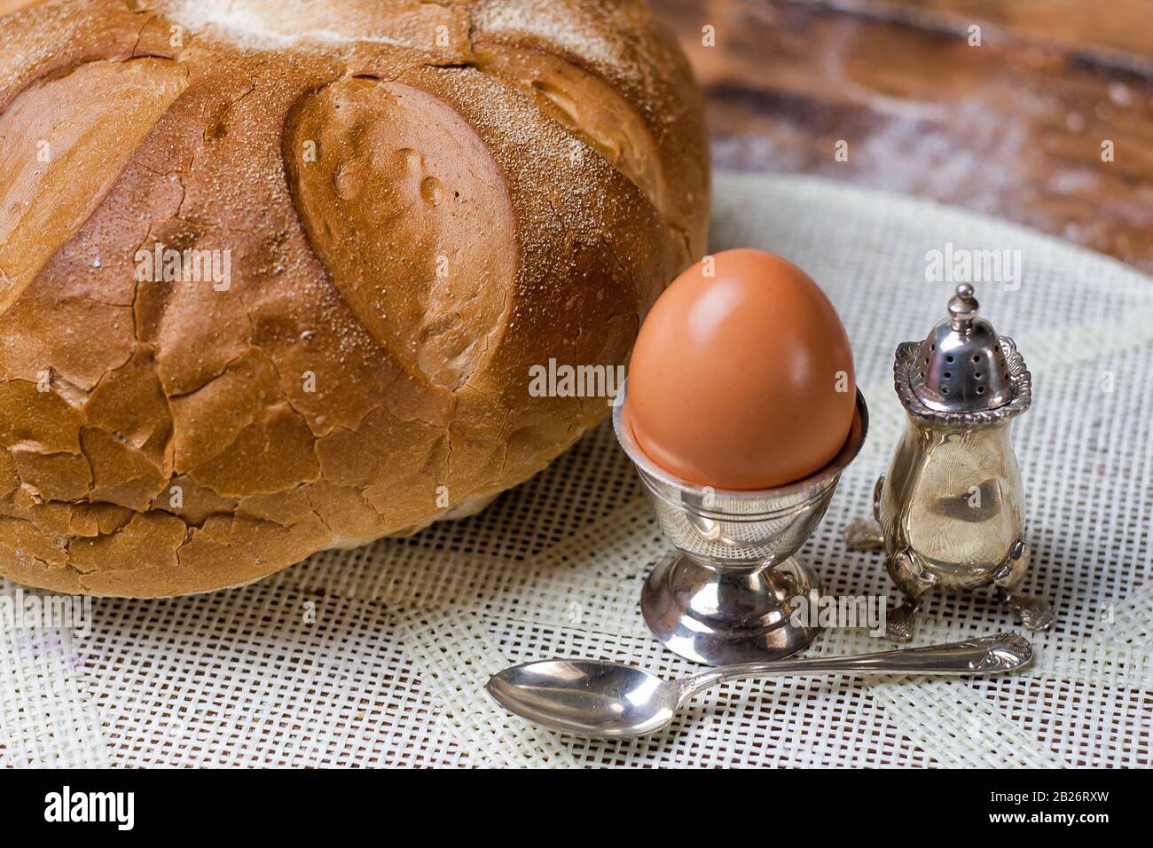 Brot auf dem Holztisch mit Mehl, Ei in silberfarbenem Vintage-Utensil, Salzschüttler und Löffel Stockfoto