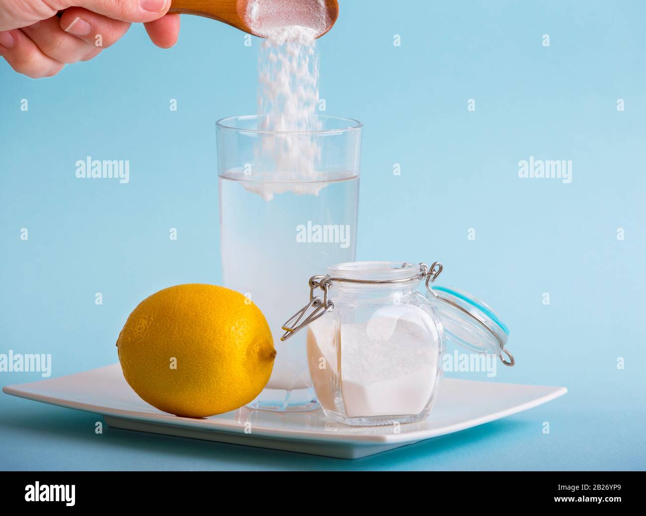 Handgießen von Backsoda im Trinkglas mit Wasser und Zitronensaft, gesundheitliche Vorteile für das Verdauungskonzept. Blauer Hintergrund, Kopierbereich. Stockfoto