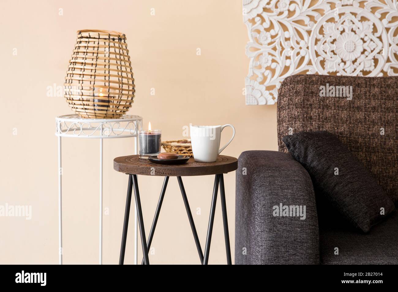 Modernes, minimalistisches Wohnzimmer mit dekorativen Elementen im asiatischen Stil. Geschnitzte Wandtafel, Bambuskerze Laterne, kleiner Holzseitentisch. Stockfoto