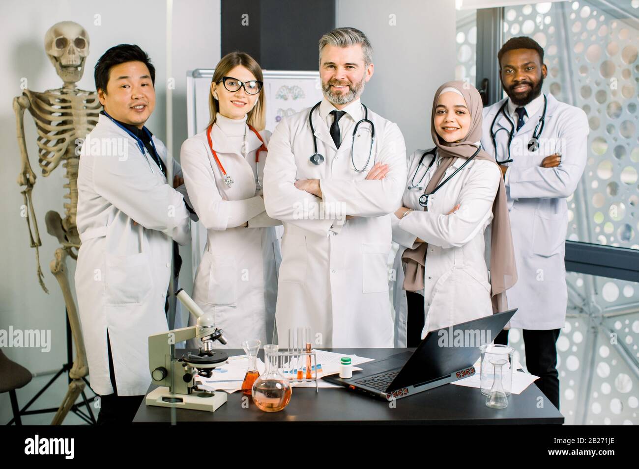 Lächelnde multiethnische Gruppe von Ärzten, Wissenschaftler im modernen Labor mit leitender männlicher Führungskraft. Team von jungen Ärzten mit reifen Einwohnern oder Studenten Stockfoto