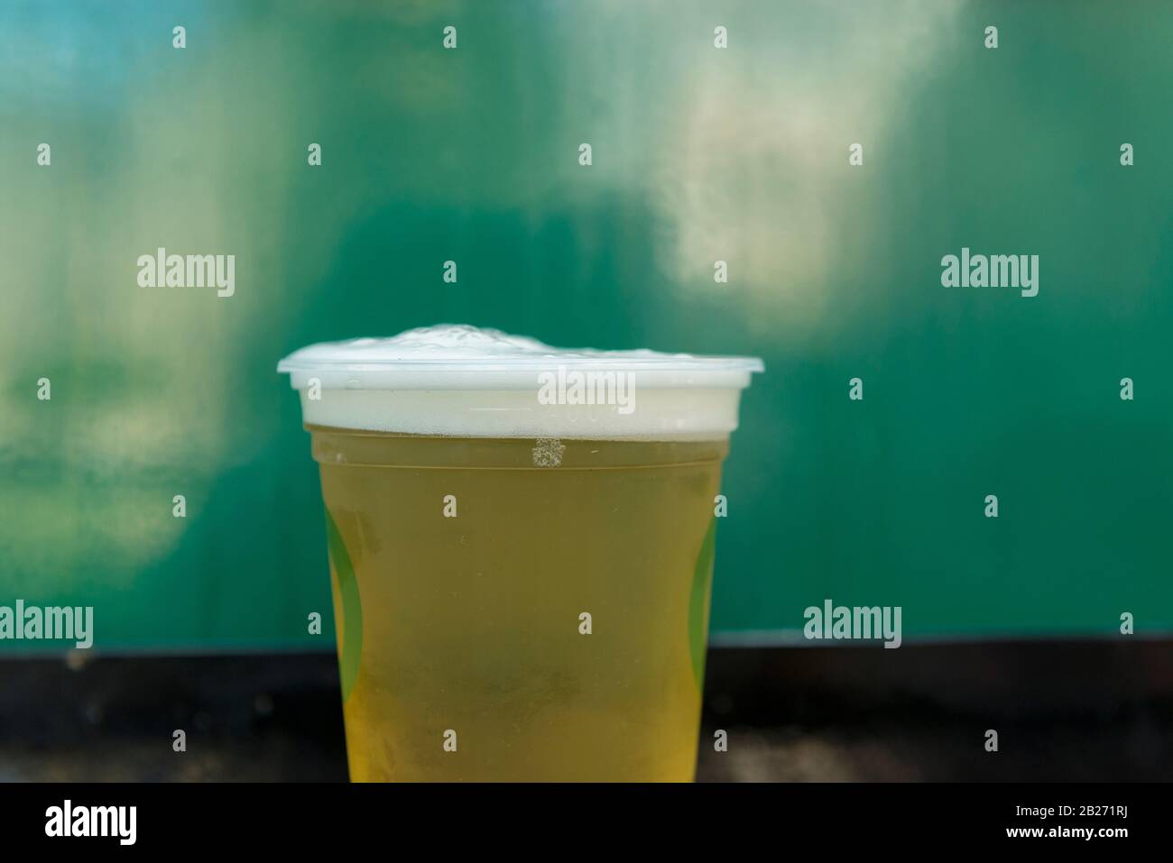 Nahaufnahme von kaltem Bier aus Kunststoffglas auf grünem Hintergrund. Golden Beer, Ale oder Lager eine Einweg-Tasse aus Kunststoff für Party auf schwarzem Metall-Tablett Pilse Stockfoto