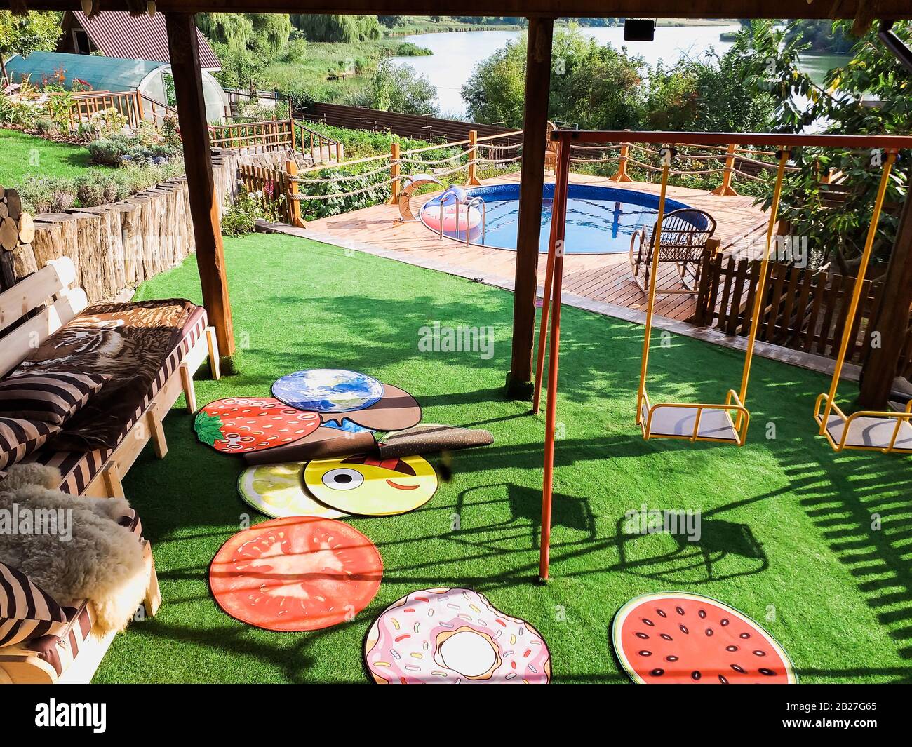Schwimmbad mit Treppe und Holzterrasse im Hotel. Blick auf den Pool und den Fluss von einer grünen Wiese. Das Konzept der Ankunft des Sommers Stockfoto