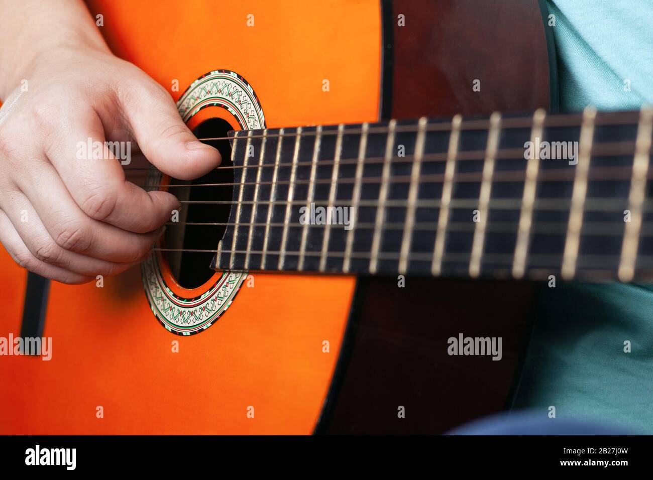 Männliche Hand spielt akustische Gitarrensaiten, die lernen, ein Musikinstrument in oranger Farbe in Nahaufnahme zu spielen. Stockfoto