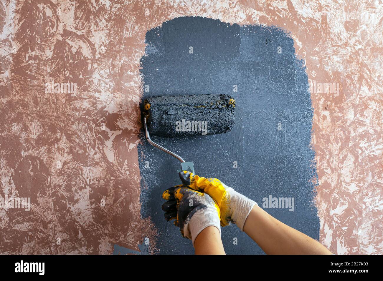 Lackierung der Wand mit einem walzengrauen Lack, Lackierung mit gelben Arbeitshandschuhen, Reparatur von Lackierwerkzeugen. Stockfoto