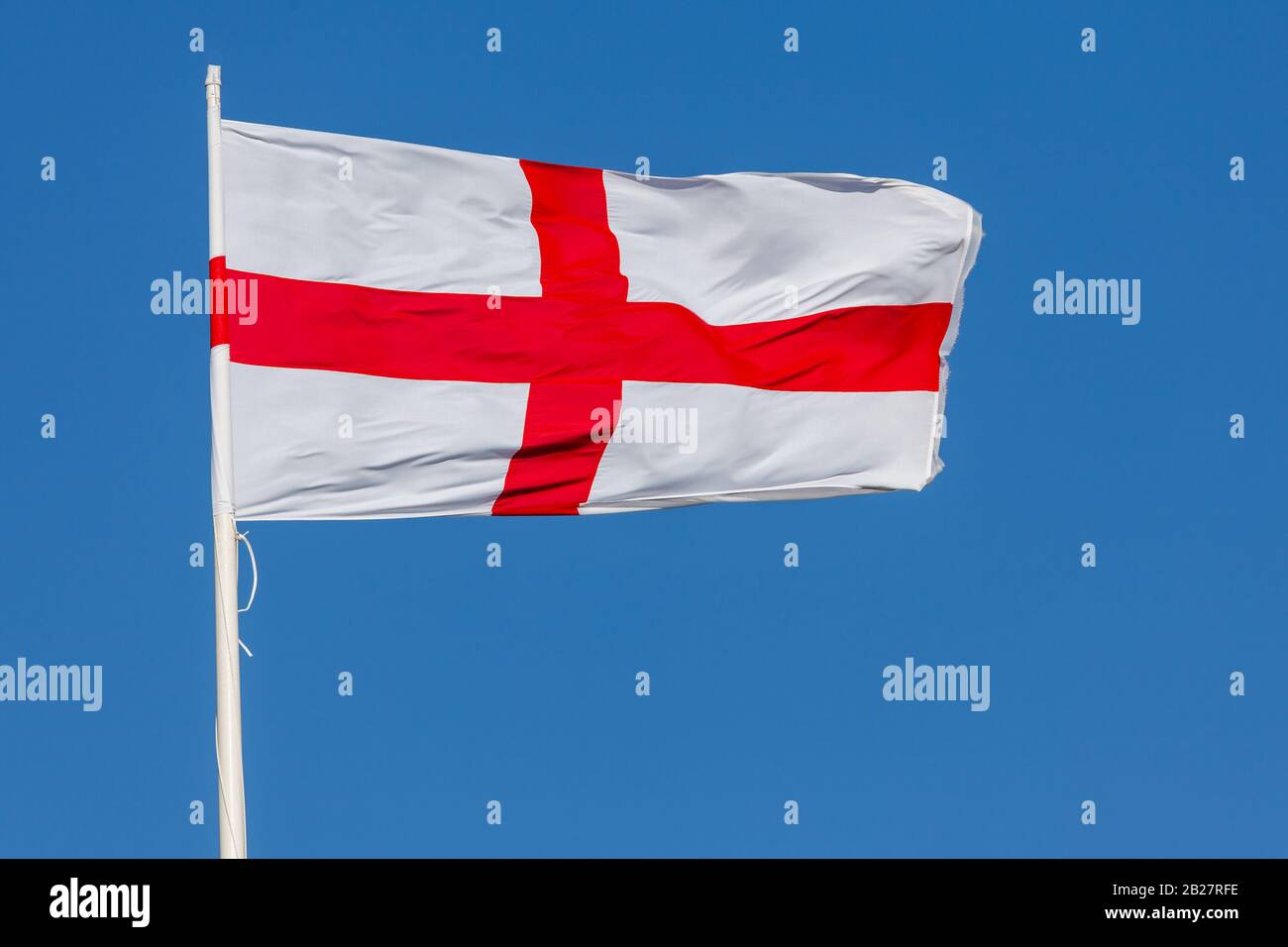 Flagge des heiligen Georg von England, die im Wind auf einem Fahnenmast mit blauem Himmel fliegt. Rotes Kreuz auf weißem Hintergrund Stockfoto