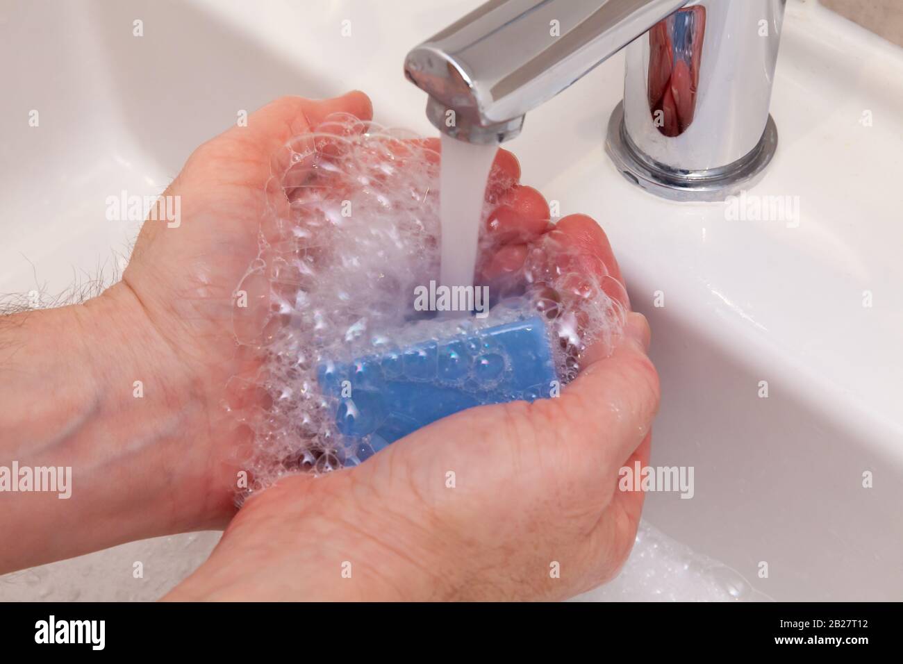 Waschen der Hände mit Seifenlauge unter fließendem Wasser aus einem Chrom-Hahn und einem Waschbecken. Stoppen Sie das verbreiten von Viren, Keimen und Bugs Konzept Stockfoto