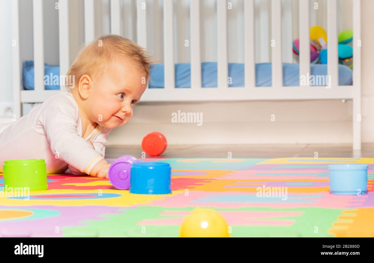 Kleine Kleinkinder schleichen sich auf dem Boden des Kindergartens mit bunten Spielzeugen Stockfoto