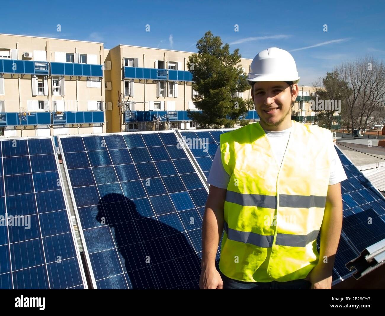 Kaukasisch attraktiver junger Techniker mit Blick auf die Kamera neben den Sonnenkollektoren. Alternative Stromquelle, nachhaltige Ressourcenkonzeption. Stockfoto