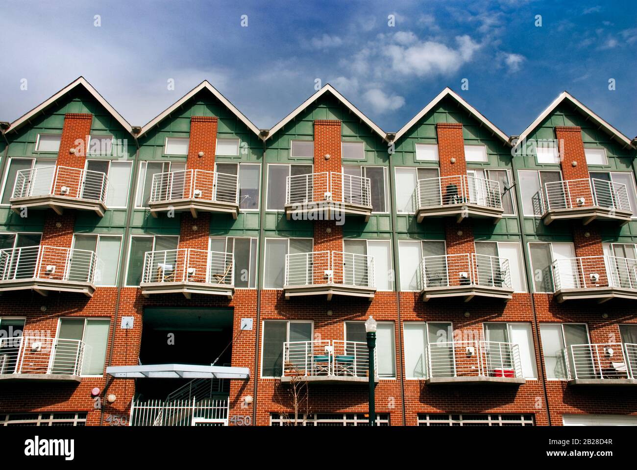 Gerader Blick auf einen roten Ziegelstein und ein grünes Holz drei übereinander gestapelte Apartmentkomplex mit kleinen individuellen Balkons auf der Terrasse und mit mehreren Dachpoint-Punkten Stockfoto