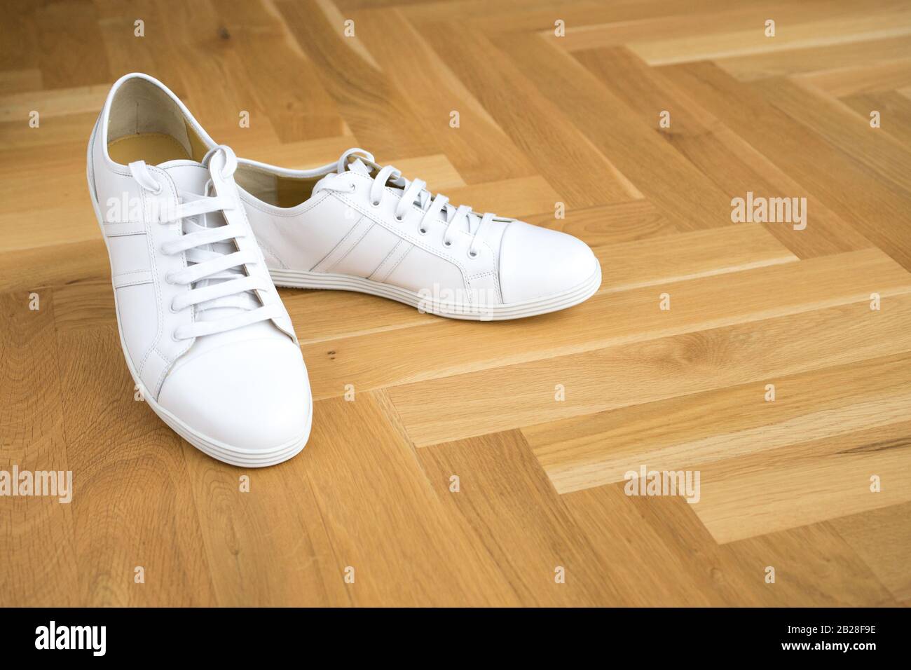 Trendige Sneaker aus weißem Grundleder auf Holzboden, bequeme Lederschuhe, modernes Outfit Stockfoto