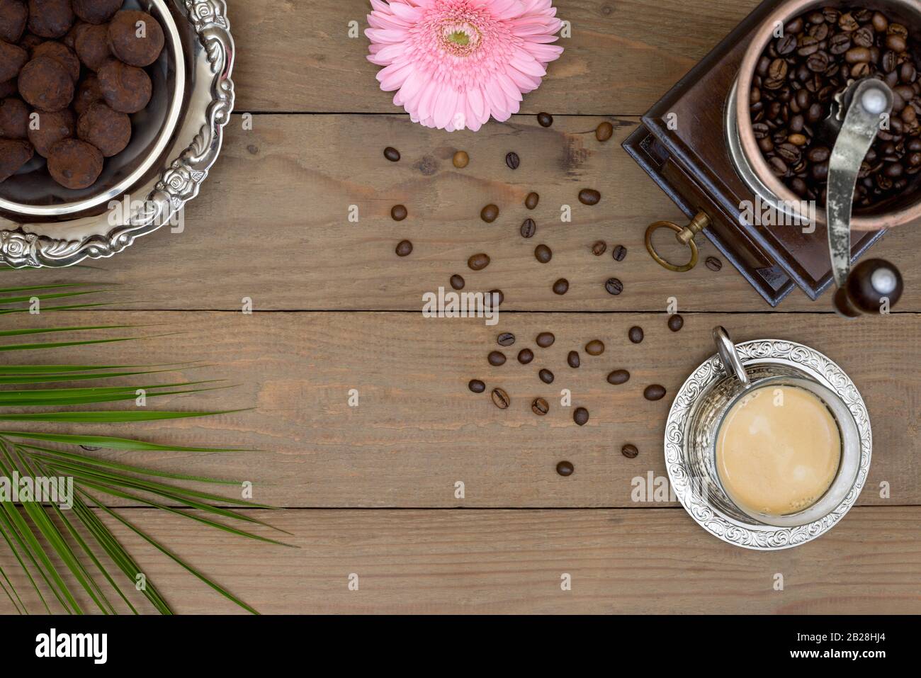 Vintage manuelle Kaffeemühle, Kaffeebohnen, Retro-Metallbecher mit Kaffee, silberne Metallplatte mit Schokoladentrüffel und rosa Gerbera Daisy Blume mit Stockfoto
