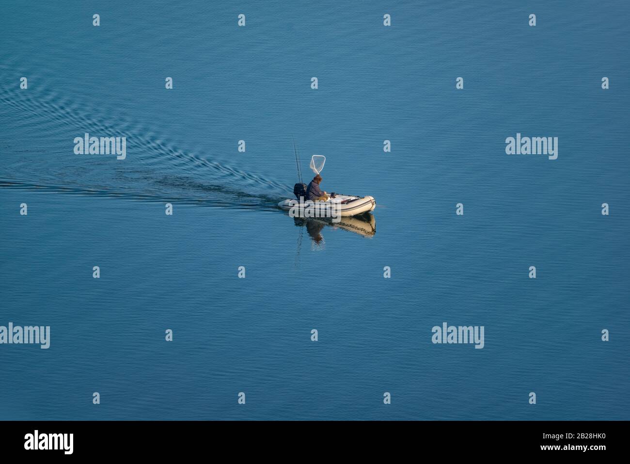 Fischer in der Mitte des blauen Sees Angeln auf einem Gummi aufblasbaren Motorboot. Stockfoto