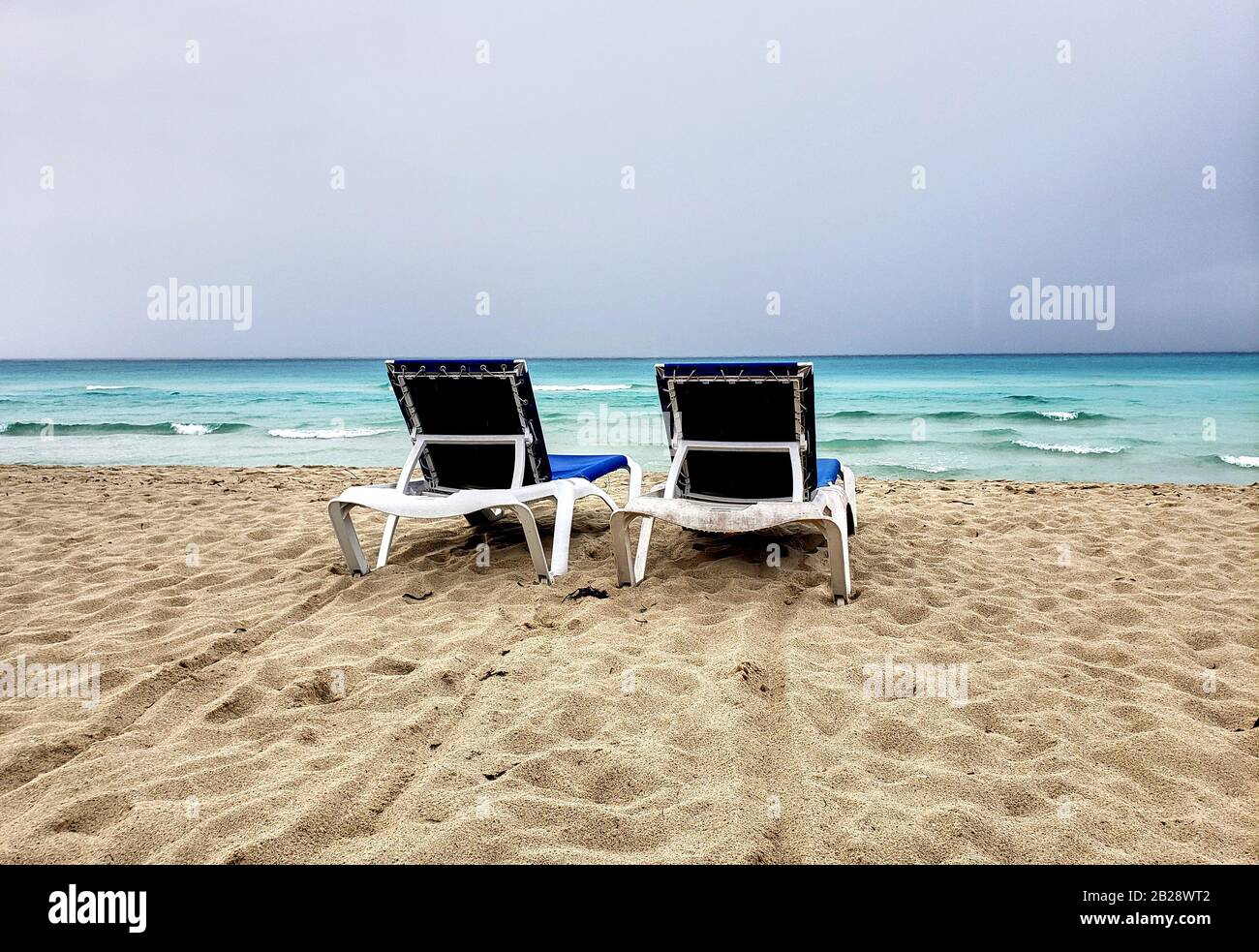 Zwei liegen, Chaiselongues an einem kubanischen Strand vor dem Sturm. Bewölktes und windes Wetter und Himmel. Stockfoto
