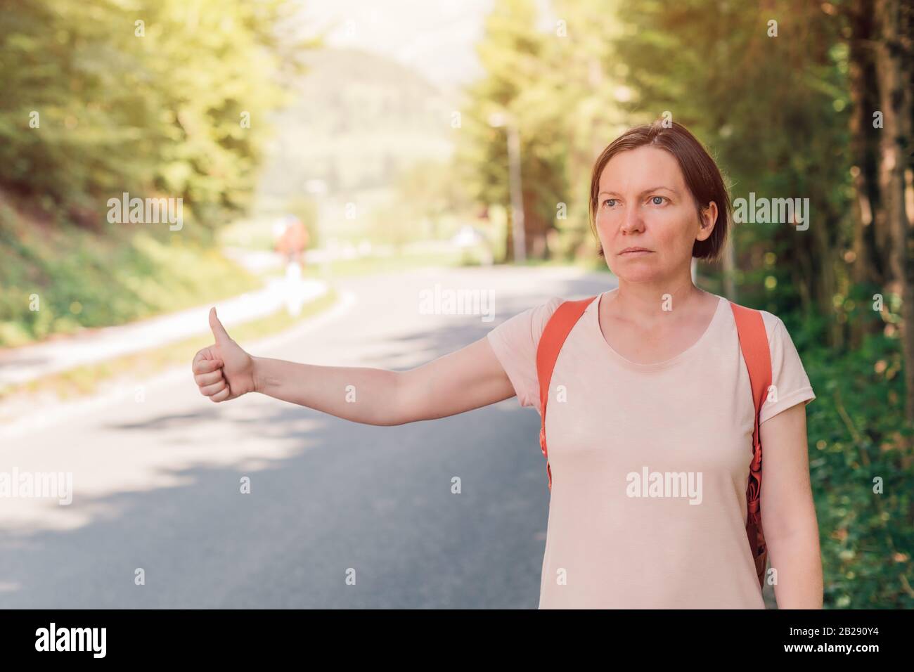 Weibliche Wanderer per Anhalter auf der Straße durch die Landschaft auf sonnigen Sommertag Stockfoto