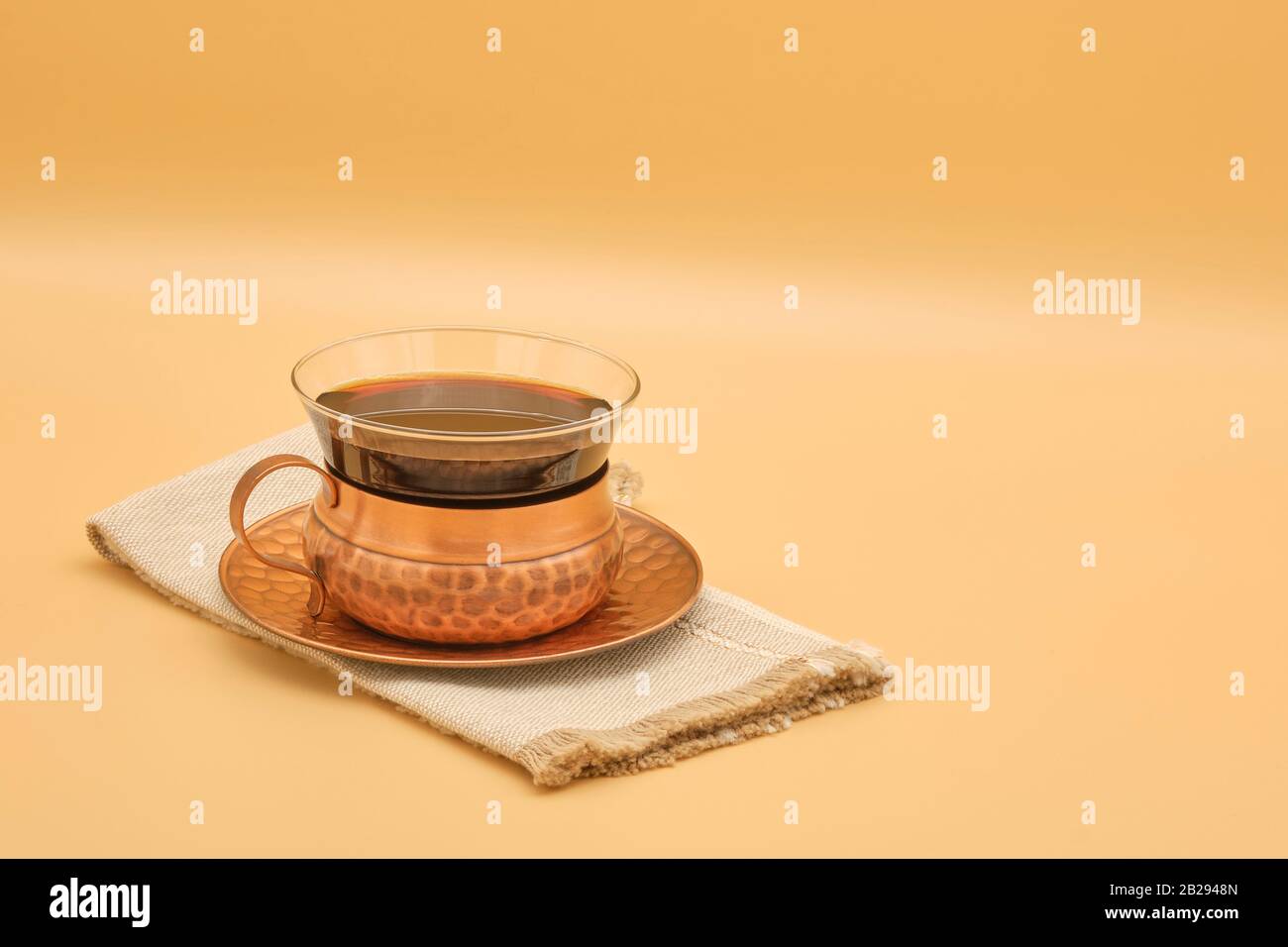 Tasse schwarzen Kaffees in einer schönen, gehämmerten Kupferschale und Untertasse, die auf einem neutralen Hintergrund mit viel Platz für Kopien fotografiert wurde. Stockfoto