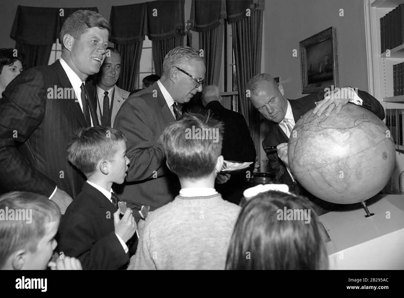 Als er die Route seines Orbitalflugs zeichnete, signiert Astronaut Oberstleutnant John H. Glenn, Jr. (rechts) bei einem Empfang zu seinen Ehren den "Fliers' and Explorers' Globe" der American Geographical Society (AGS) im Oval Office of the White House. Präsident John F. Kennedy (ganz links), Vizepräsident Lyndon B. Johnson (hinten), AGS-Direktor Charles B. Hitchcock (im Profil, mit Brille) und mehrere Kinder, darunter Präsident Kennedys Neffe Robert F. Kennedy, Jr. (im Vordergrund, zweite von links), sehen von links. Stockfoto