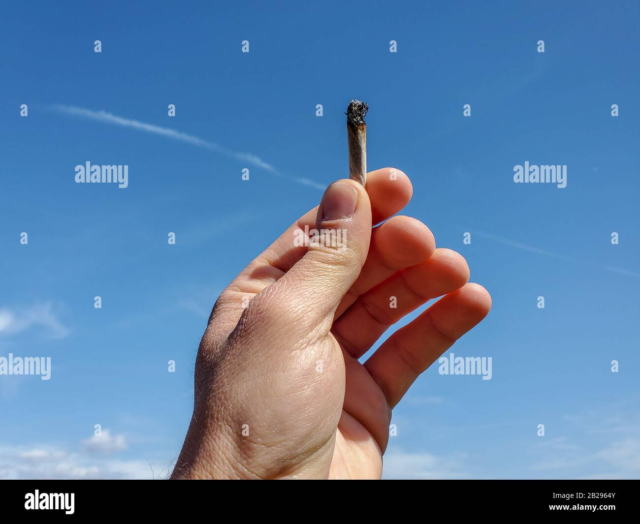 Menschliche Hand hält Tabakzigarette auf blauem Himmel, rauchsüchtig Stockfoto