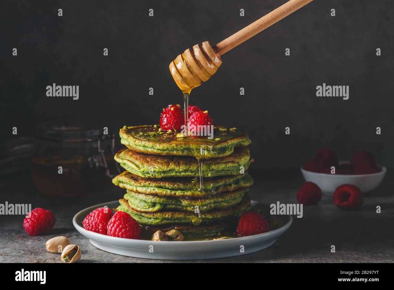 Matcha-Grünpfannkuchen mit frischen Himbeeren, Pistazien und fließendem Honig auf dunklem Hintergrund. Low Key. Gesundes Frühstücksdessert. Vintage-Tönung Stockfoto