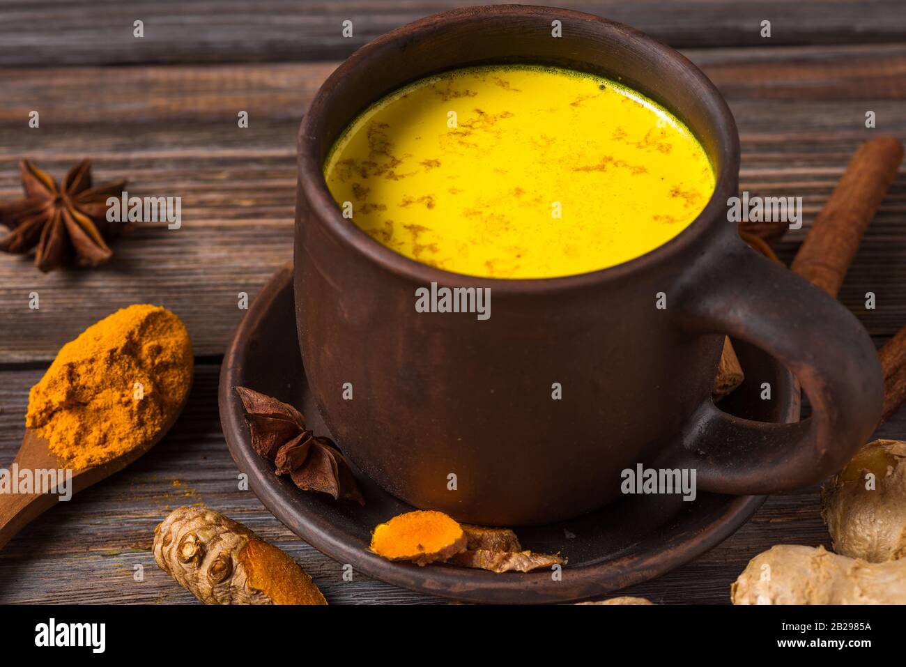 Traditionelle indische Getränke turmreiche Latte oder goldene Milch mit Zimt, Ingwer, Anis, Pfeffer und Kurkuma auf rustikalem Holztisch. Gesundes Getränk Stockfoto