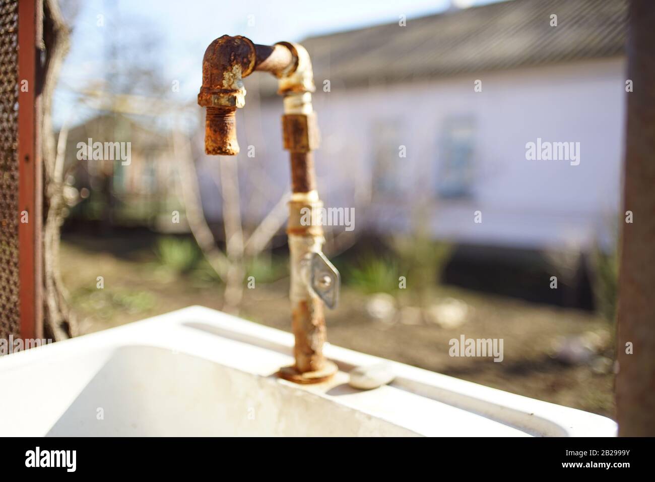 Altes rostiges Wasser trank auf einem Waschbecken in einem ländlichen Hof. Die Fassade des Hauses im Hintergrund verwackelt. Sonniger Tag Stockfoto