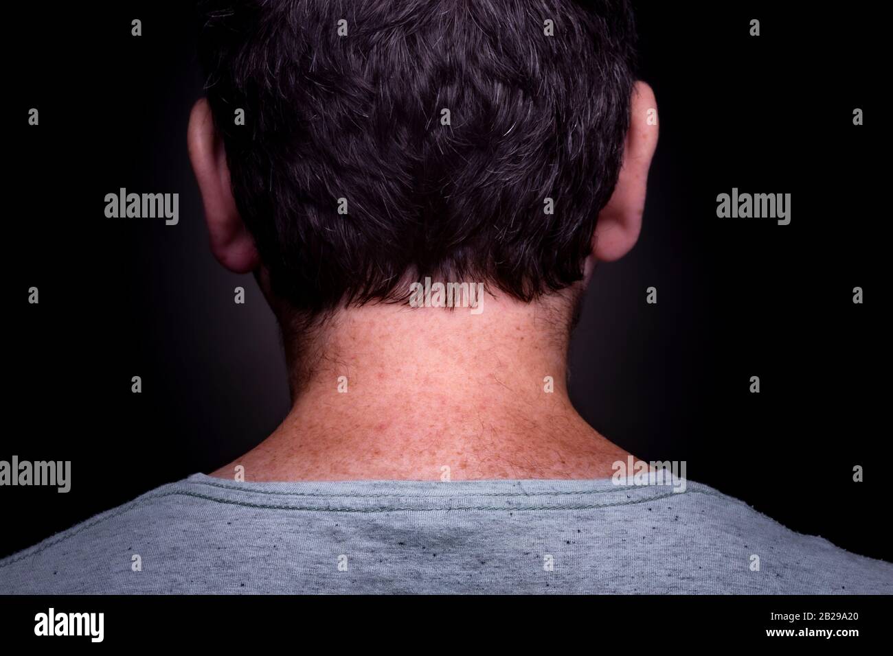 Anonymer kaukasischer Mann mit kurzem braunem Haar und graugrünem Hemd an und freckelt in seinem Nacken von hinten vor dunklem Hintergrund Stockfoto