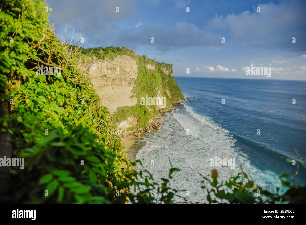 Wellen, die in Richtung einer Klippe nahe dem Uluwatu-Tempel auf Bali mit bewölktem Himmel im Hintergrund während eines späten Frühlingsnachmittags stürmen Stockfoto