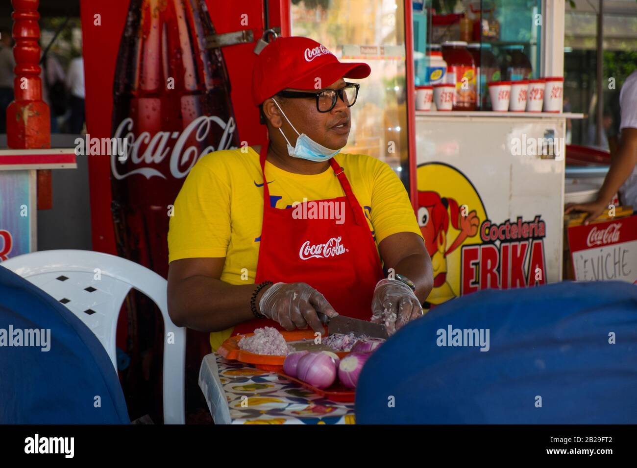 Ein Mann trägt eine Gesichtsmaske, während er auf einem Lebensmittelstand in Cartagena, Kolumbien, Zwiebeln für Ceviche hackt Stockfoto
