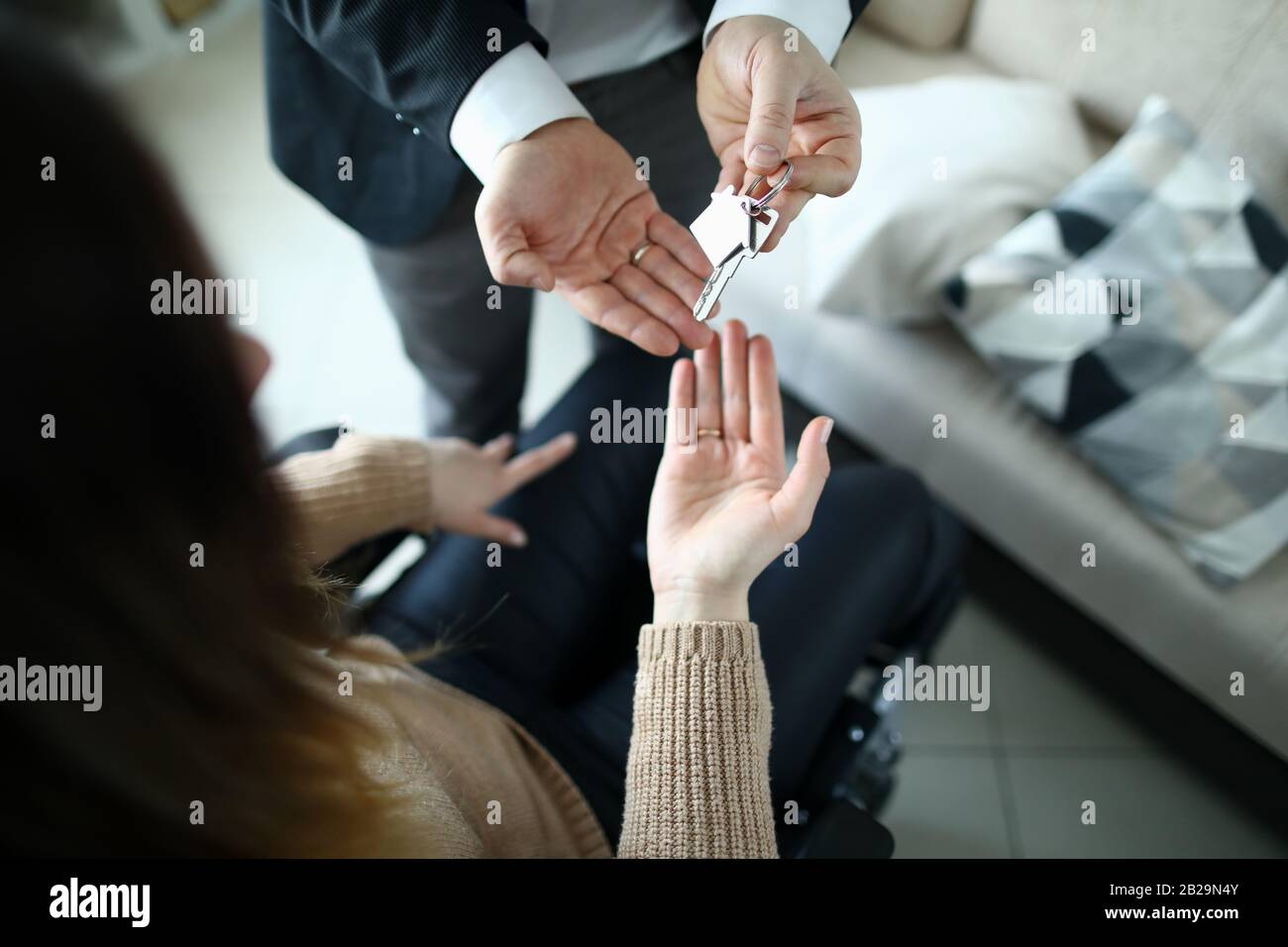 Die Hand eines männlichen Geschäftsmannes gibt den Schlüssel an eine Frau aus neuem Gehäuse weiter Stockfoto