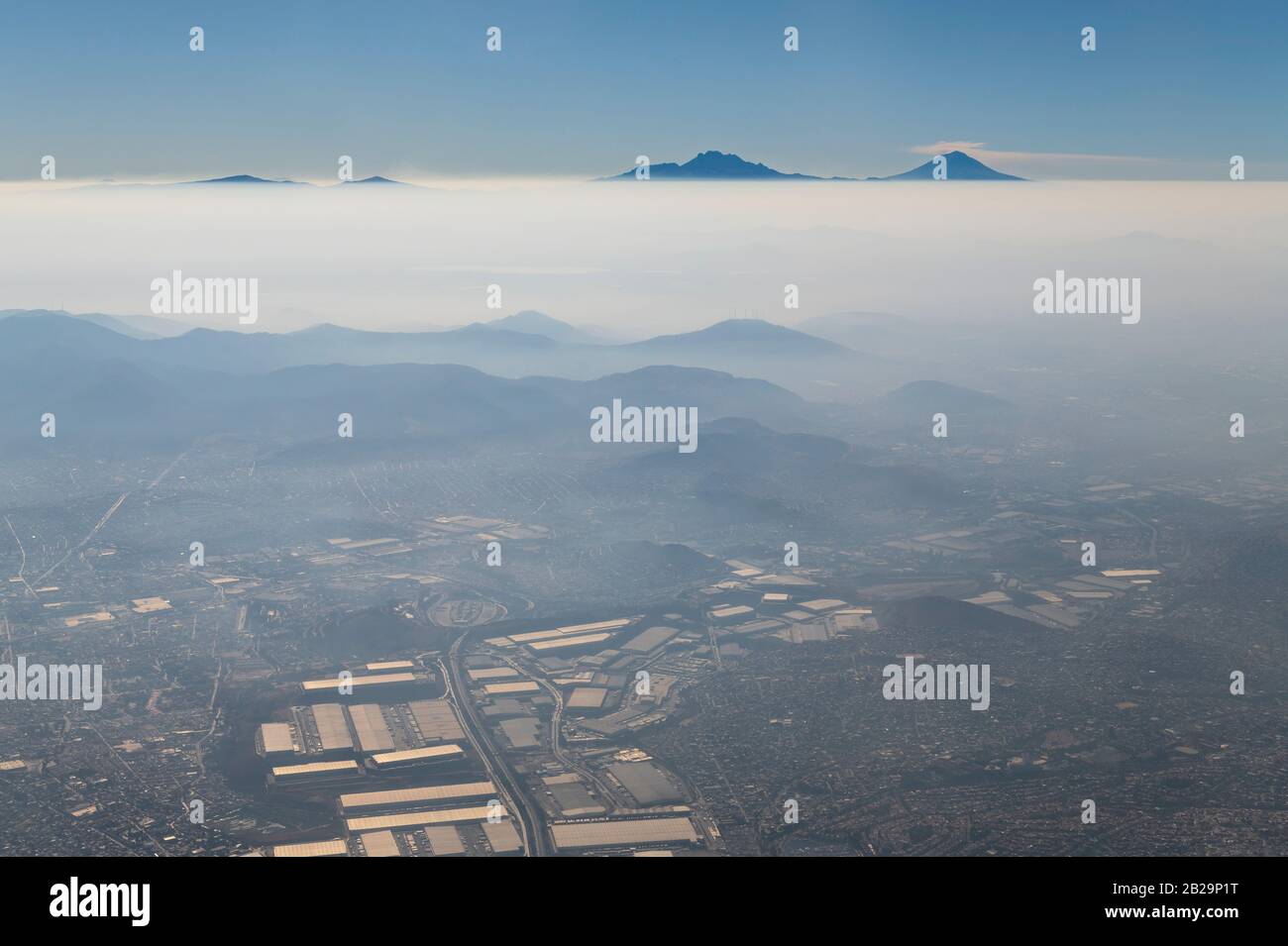 Luftaufnahme von Mexiko-Stadt im Smog und Nebel mit dem aktiven Vulkan Popocatepetl und dem ruhenden Vulkan Iztaccihuatl am Horizont, Mexiko. Stockfoto