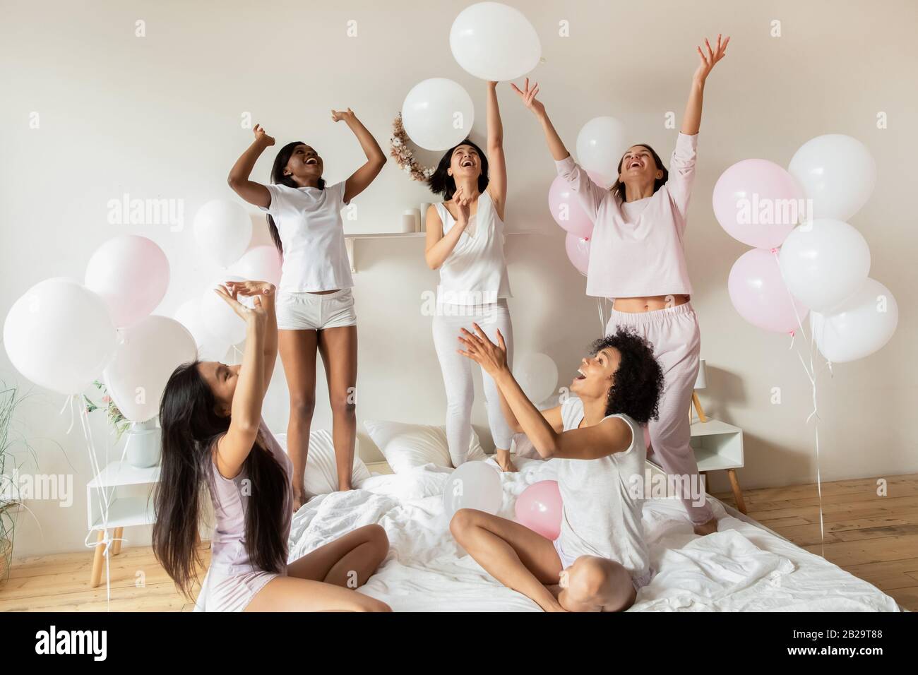 Fröhliche diverse Mädchen, die auf der Party mit Ballons im Schlafzimmer spielen Stockfoto