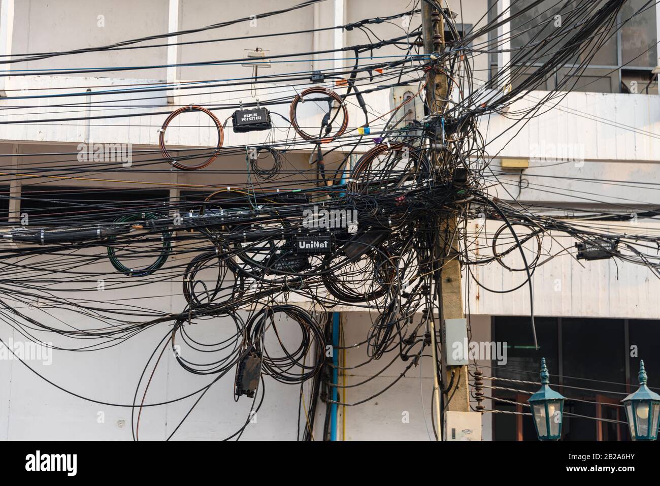 Unordentliche und unsaubere elektrische Kabel, die an einem Strompfosten in Thailand hängen Stockfoto