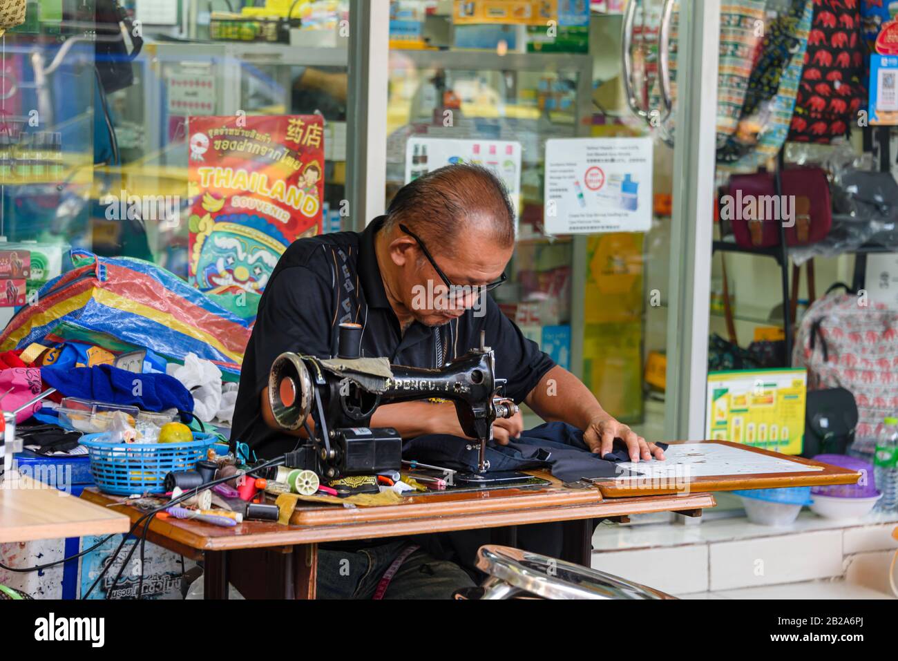 Ein Mann repariert Kleidung mit einer alten Gusseisen-Nähmaschine, Bangkok, Thailand. Stockfoto