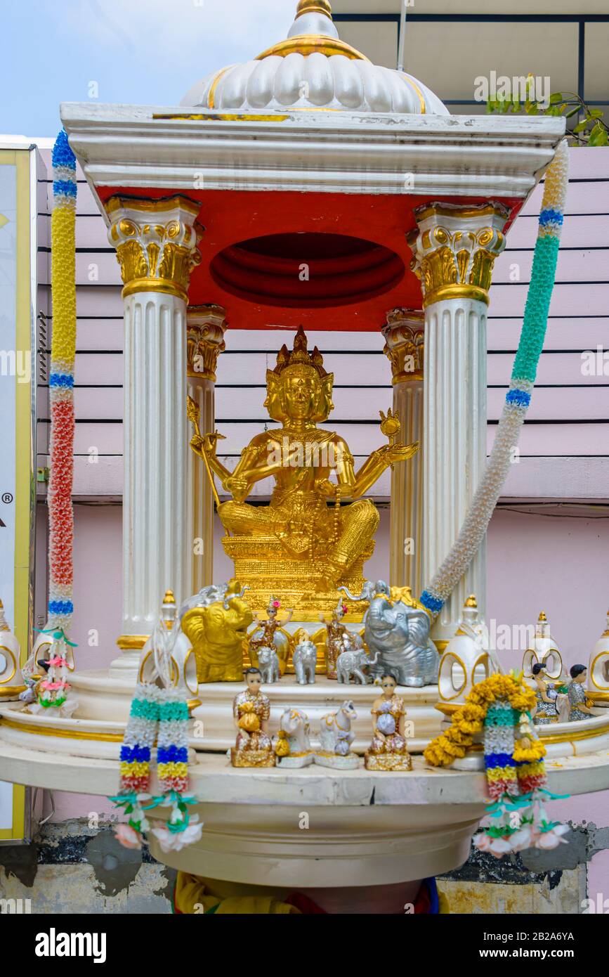 Goldene buddha-statue mit mehreren Facetes in einem Schrein mit orangefarbenen Blumen, Bangkok, Thailand Stockfoto