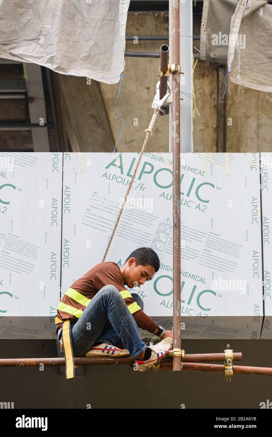 Ein Arbeiter hängt von einem Gerüstpfosten mit Sicherheitsgurt, Seil und Haken hoch über einem Baugelände, Bangkok, Thailand. Stockfoto