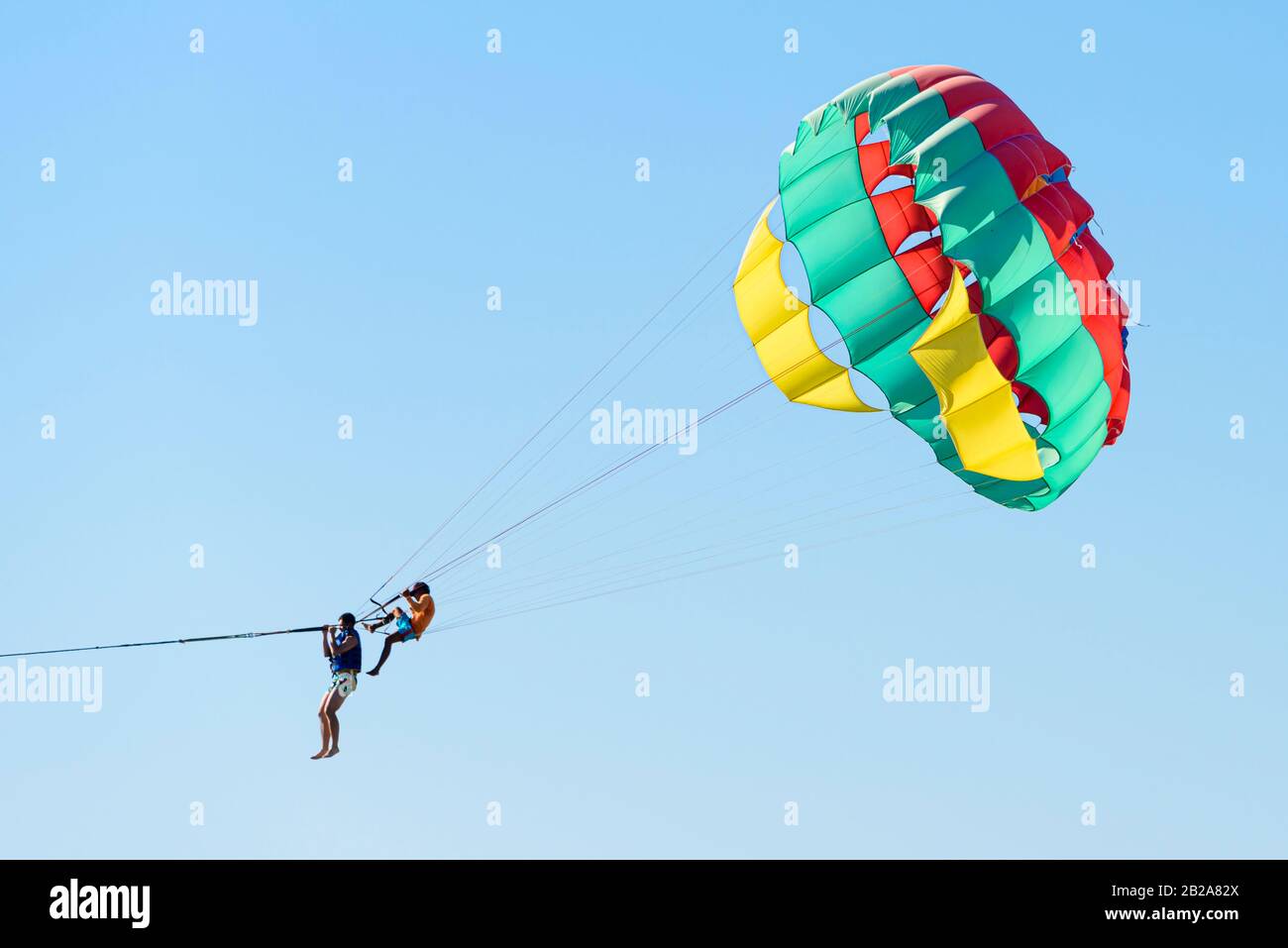 Tourist in einen Parascending Fallschirm getappt, während ein Thailänder an den Seilen sitzt und hält, Kata Beach, Phuket, Thailand Stockfoto
