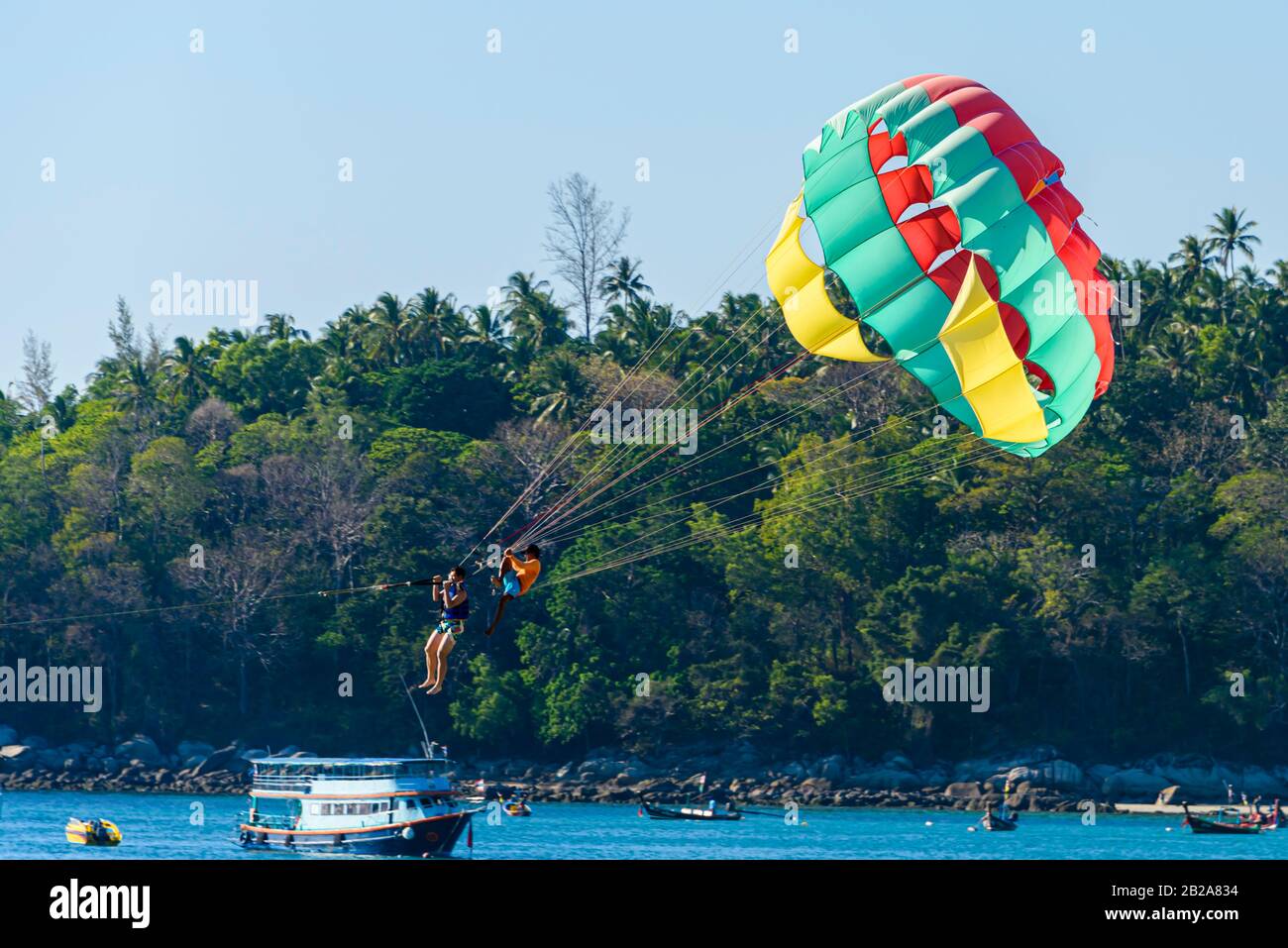 Tourist in einen Parascending Fallschirm getappt, während ein Thailänder an den Seilen sitzt und hält, Kata Beach, Phuket, Thailand Stockfoto