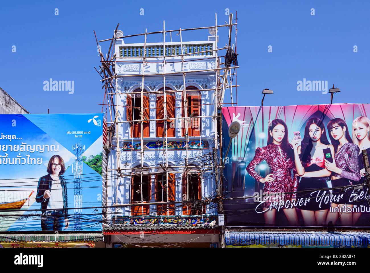 Bambusgerüste außerhalb eines traditionellen Gebäudes, das einer Reparatur unterzogen wird, umgeben von Werbetafeln, Phuket, Thailand Stockfoto