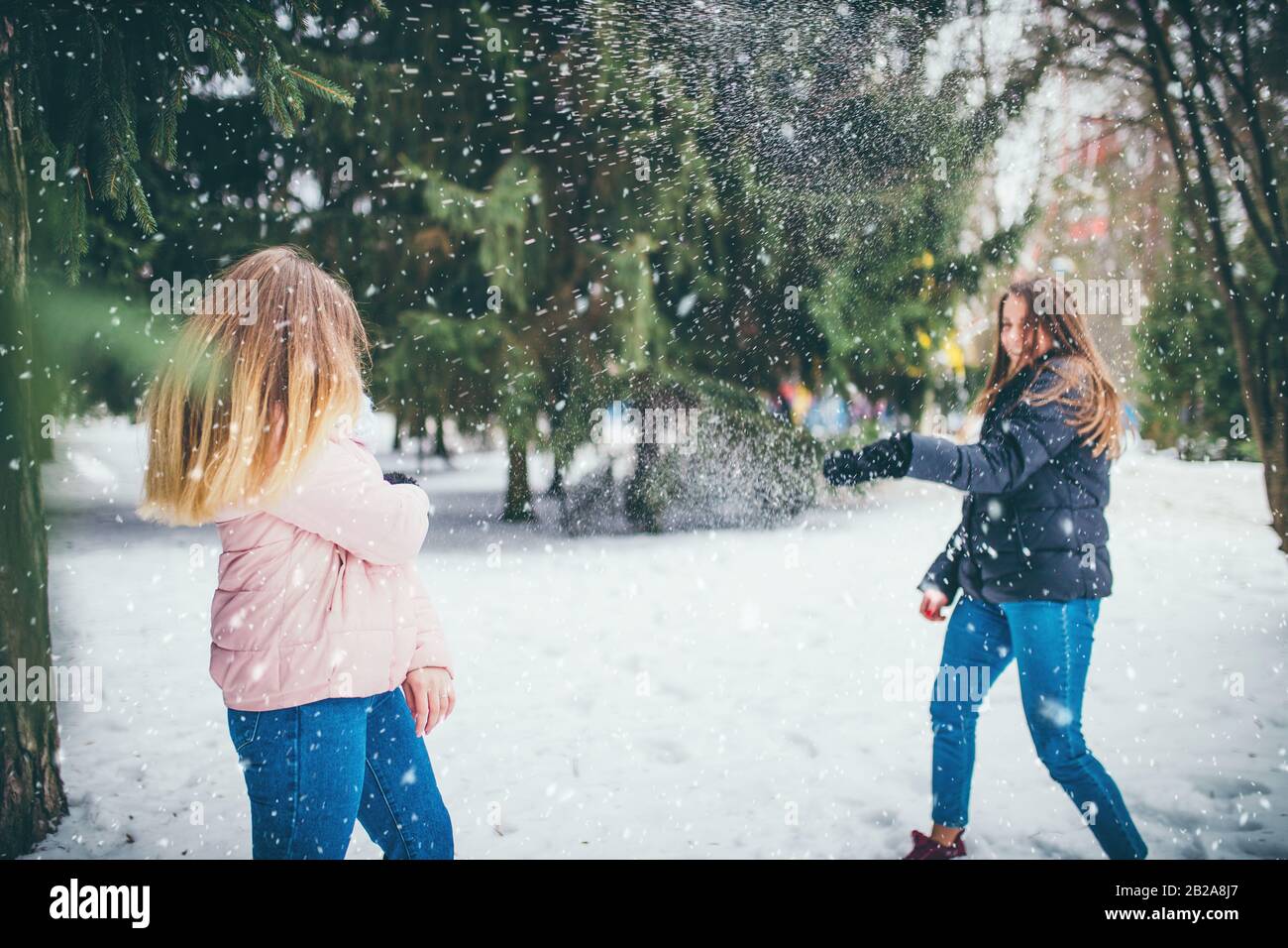 Junges Mädchen an einem Wintertag im Wald wirft einen Schneeball auf ihren Freund Stockfoto