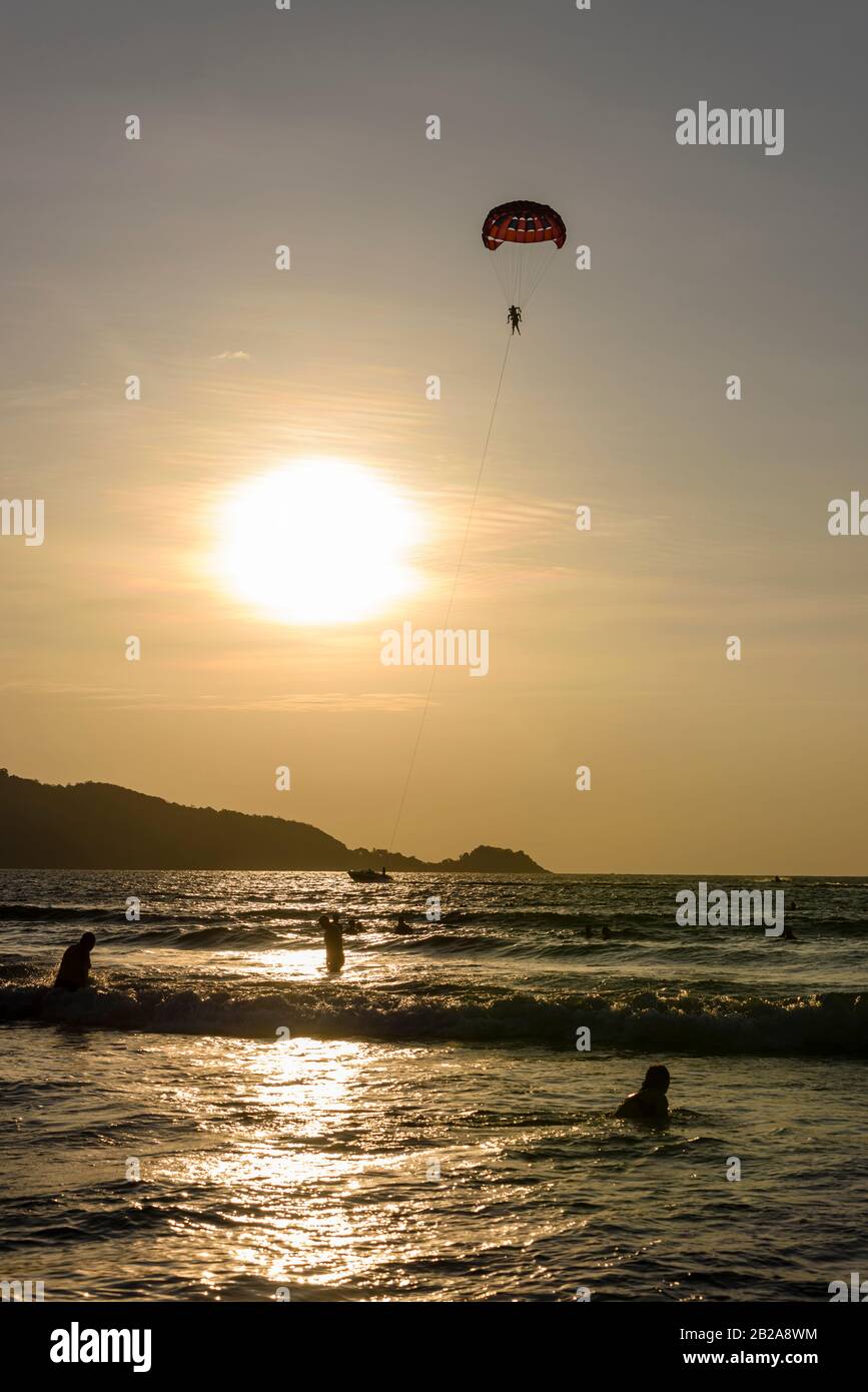 Menschen am Strand bei Sonnenuntergang, mit einem Touristenaufstieg, am Patong Beach, Phuket, Thailand Stockfoto