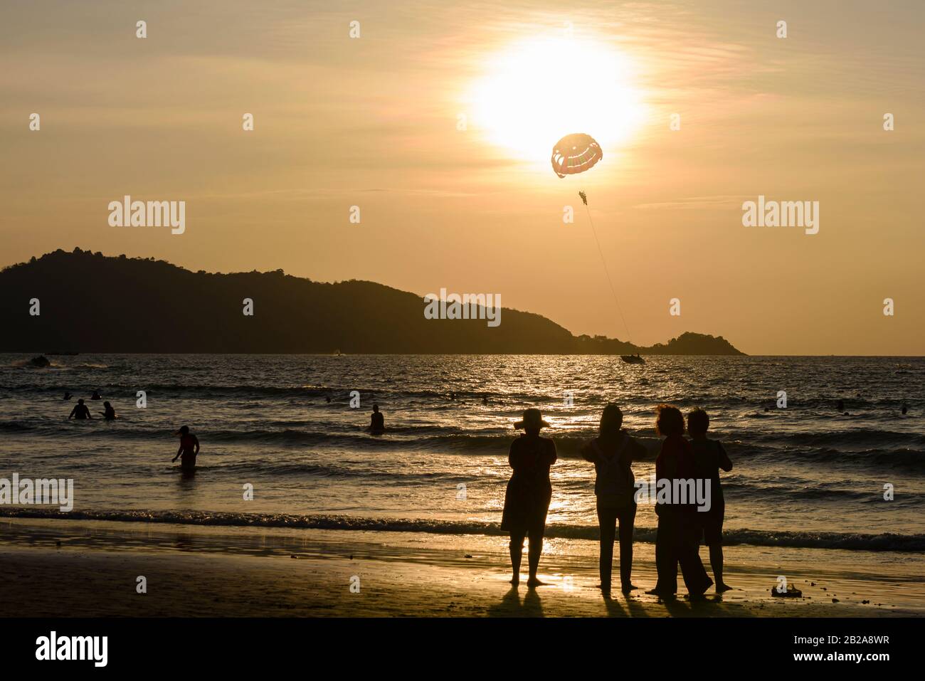 Menschen am Strand bei Sonnenuntergang, mit einem Touristenaufstieg, am Patong Beach, Phuket, Thailand Stockfoto