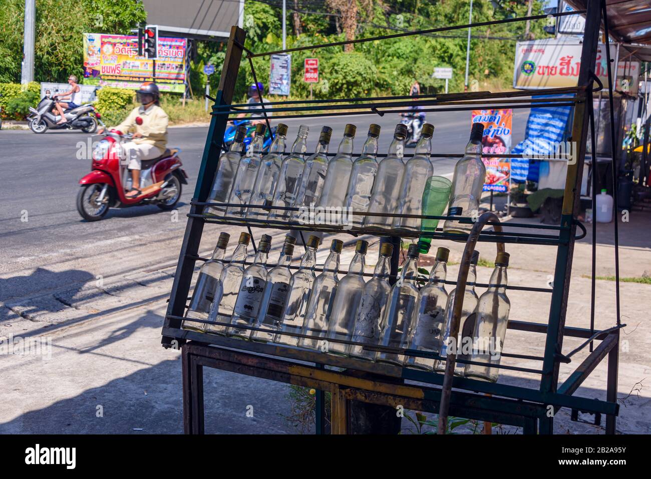 Leere Whiskyflaschen, die für den Verkauf von Litern Benzin an Rollerfahrer an der Seite der Straße in Kata, Phuket, Thailand verwendet werden Stockfoto