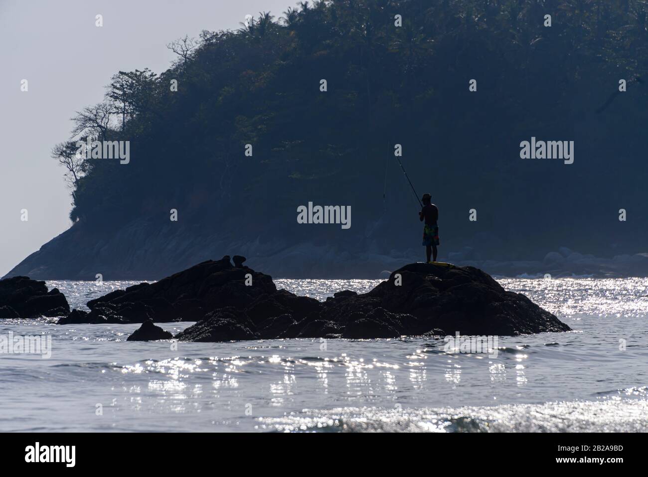 Ein Mann fischt aus Felsen mit Angelrute, Kata Beach, Phuket, Thailand Stockfoto